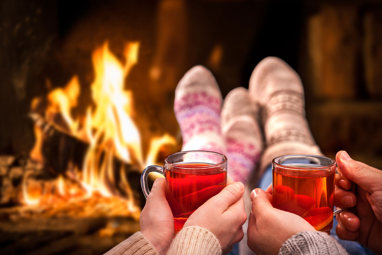 Ein Paar sitzt mit einem Getränk in den Händen in Wollsocken am Kaminfeuer.  