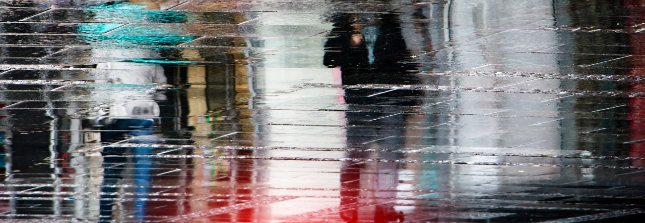 Auf regennasser Straße spiegelt sich die Stadt.
