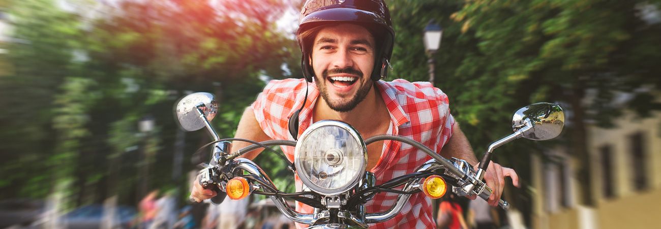 Mann mit Helm fährt auf Moped frontal Richtung Kamera