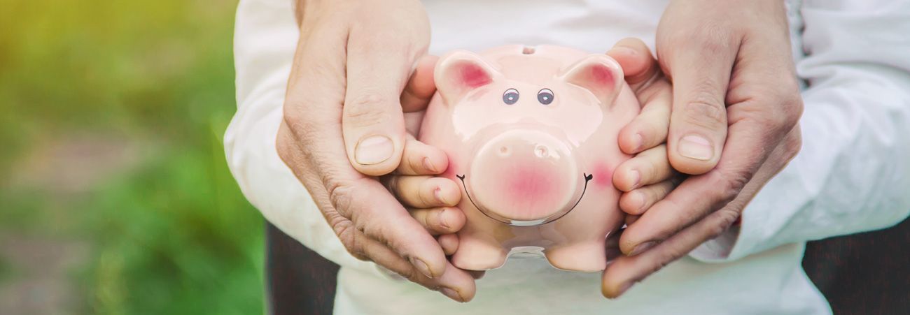 Kinderhände halten Sparschwein und werden von erwachsenen Händen umschlossen