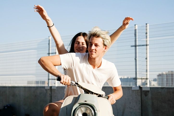 Junger Mann und junge Frau fahren zusammen fröhlich auf einem Moped