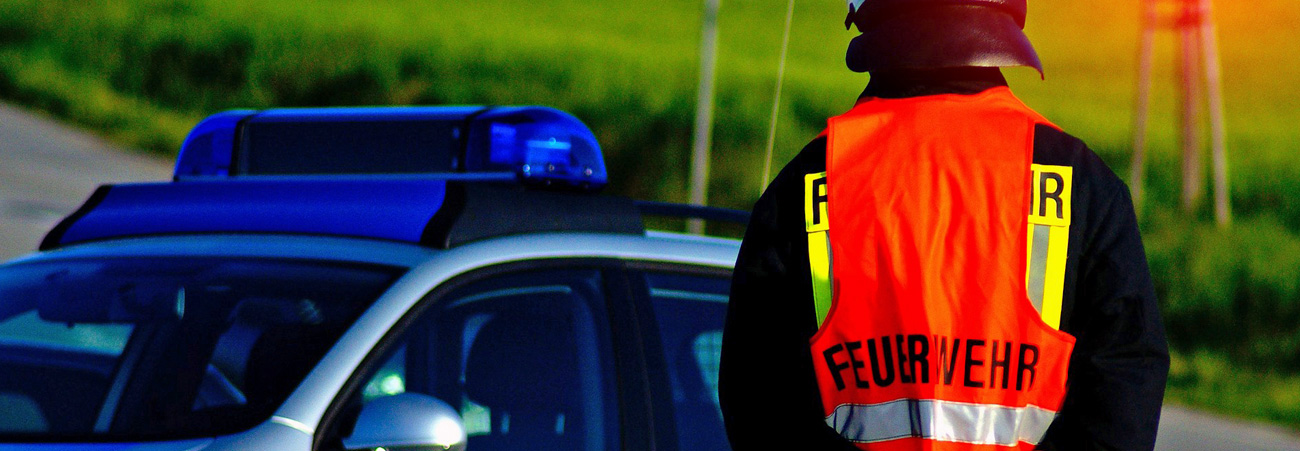Feuerwehrmann in Warnweste steht neben Einsatzfahrzeug mit Blaulicht