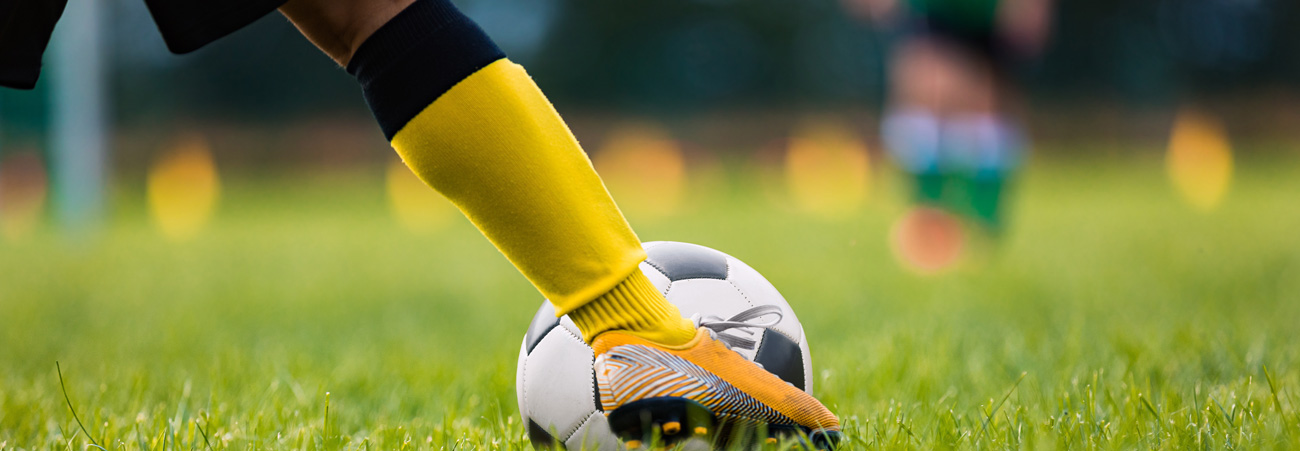 Fußballerbein mit gelben Stulpen tritt gegen einen Fußball