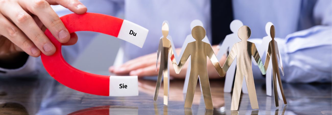 Hand hält Magnet mit Aufschrift Du und Sie und zieht Papierfiguren an