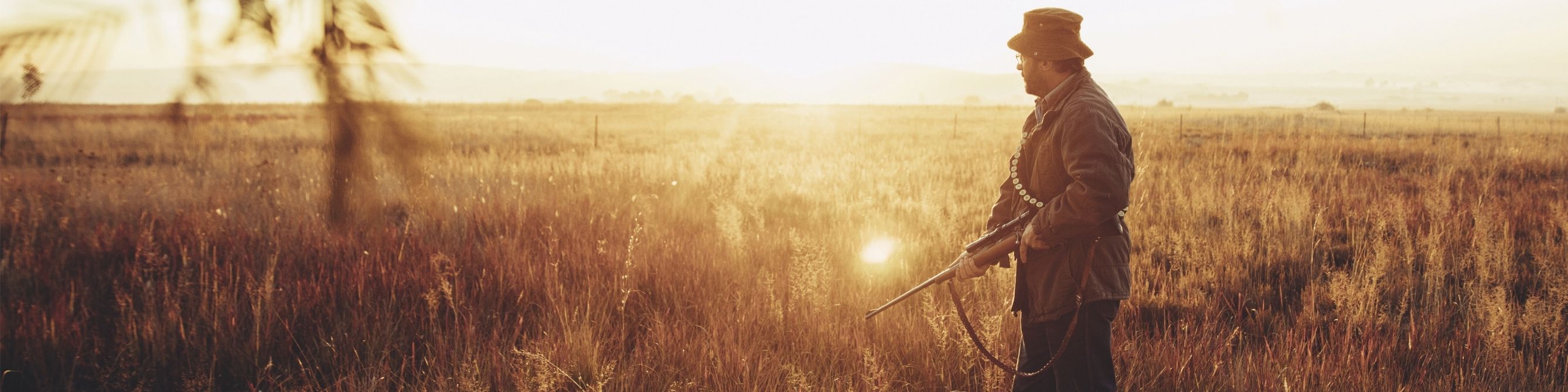 Jäger steht mit Gewehr auf einem Feld als Symbol für Jagd-Haftpflichtversicherung und finanziellen Schutz bei Schäden während der Jagd.