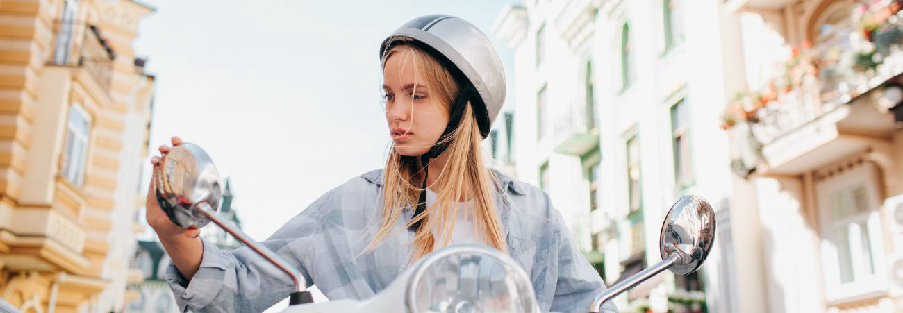 Junges blondes Mädchen sitzt auf einem Moped und stellt Spiegel ein
