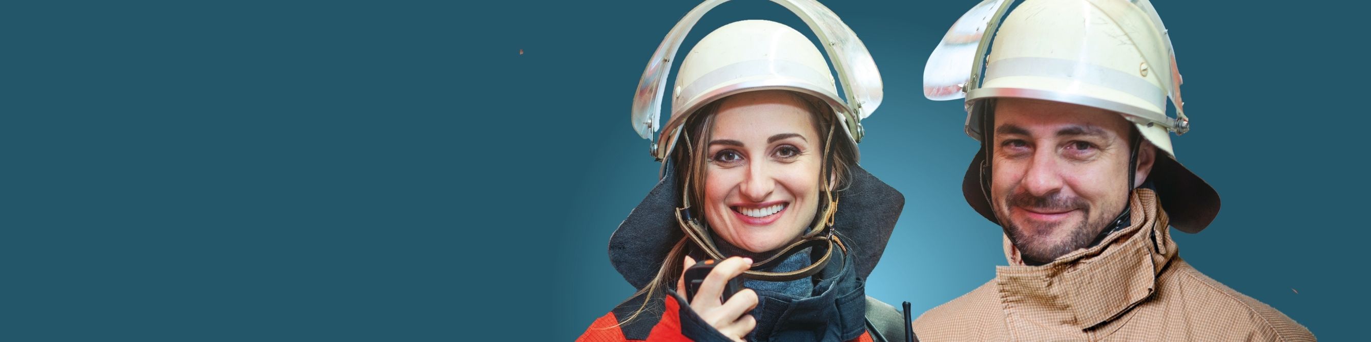 Zwei Feuerwehrleute in Schutzkleidung und Helmen stehen nebeneinander und lächeln in die Kamera