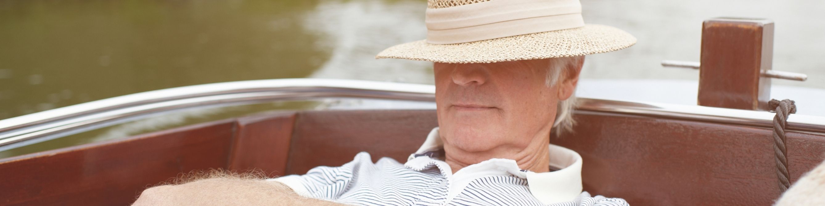 Mann mit Sonnenhut sitzt in einem Boot als Symbol für Sportboot-Haftpflichtversicherung und Schutz für Skipper und Mannschaft.