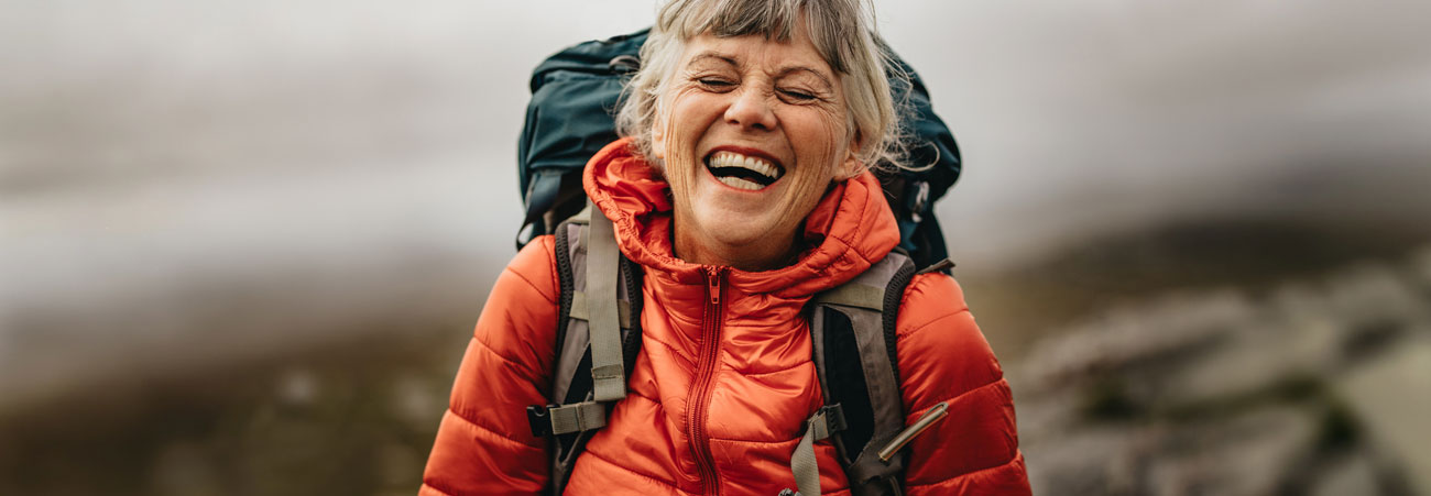 Lachende ältere Wanderin mit Rucksack und roter Jacke in der Natur – Symbol für Aktivität, Lebensfreude und Outdoor-Erlebnis
