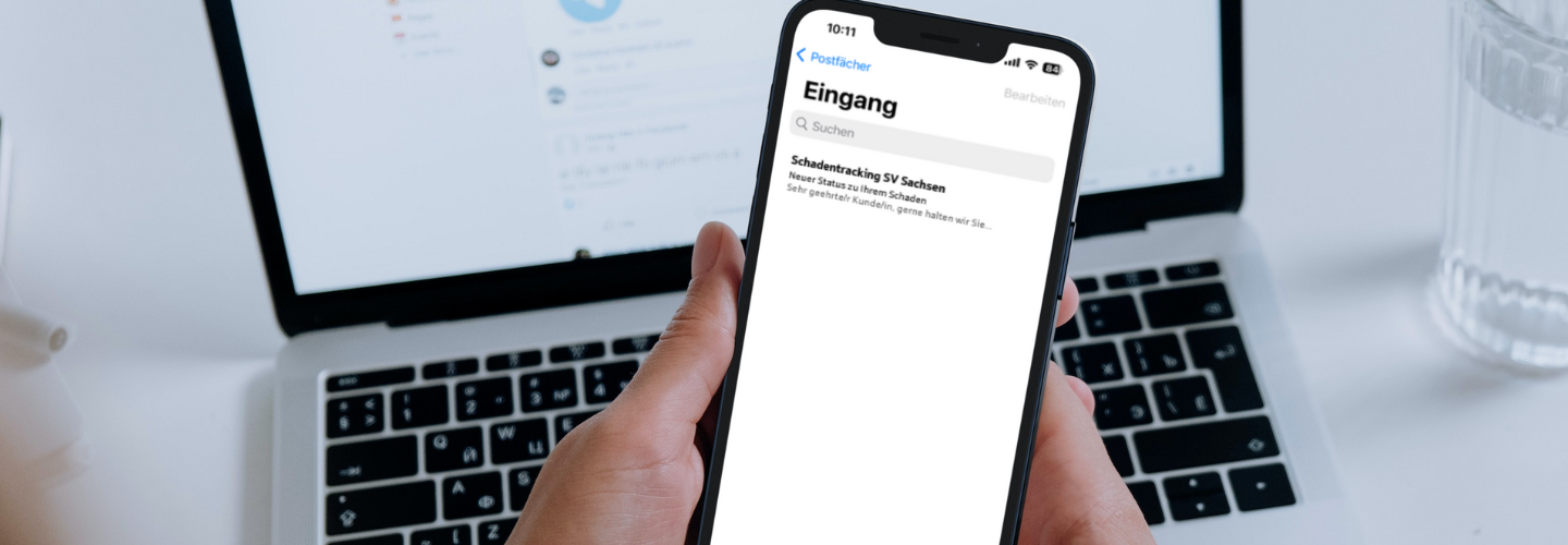 Smartphone mit Login-Bildschirm in der Hand vor Laptop