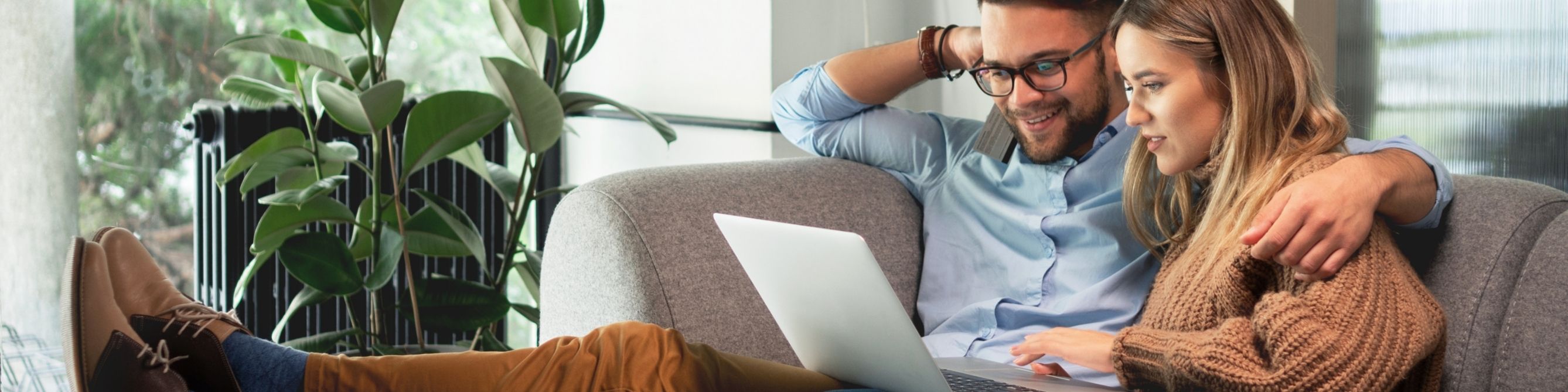 Frau und Mann sitzen auf der Couch und schauen gemeinsam auf einen Laptop.