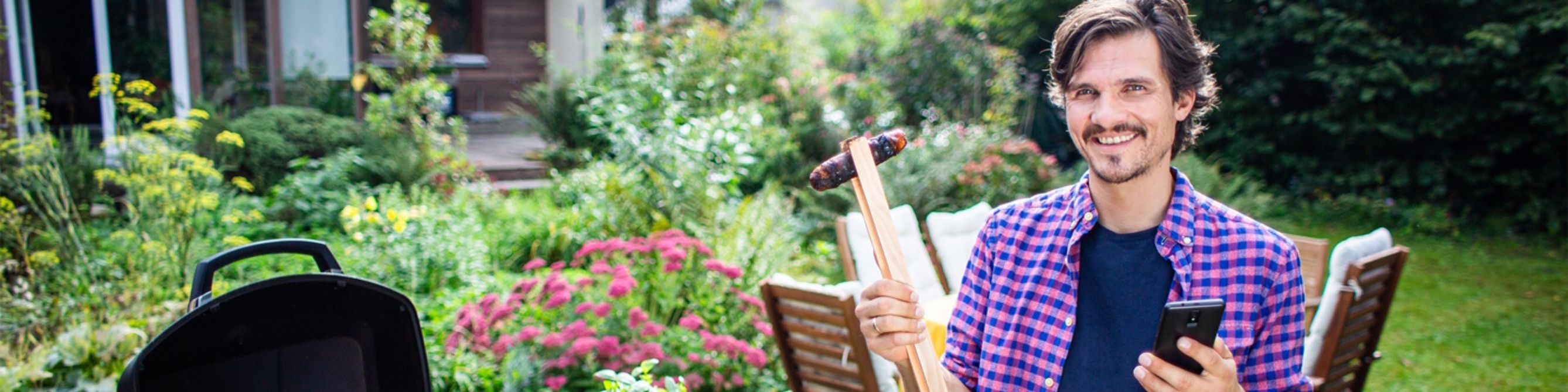 lächelnder Mann steht mit Grillzange in der Hand am Grill 