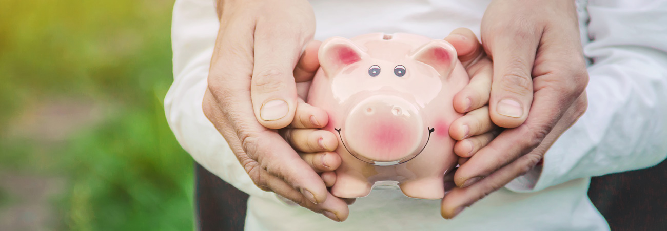 Kinderhände halten Sparschwein und werden von erwachsenen Händen umschlossen