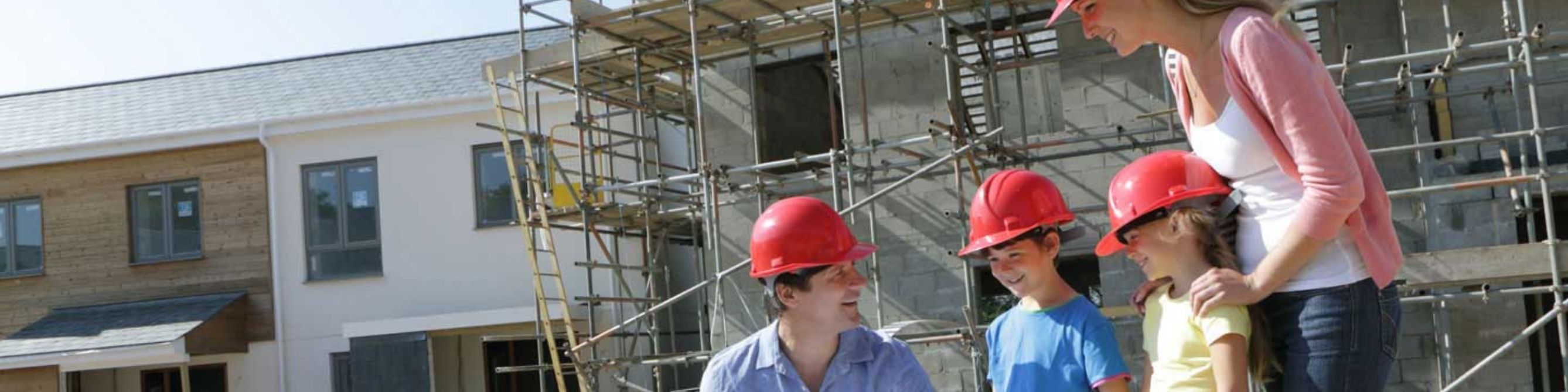 Familie steht auf einer Baustelle und betrachtet einen Bauplan