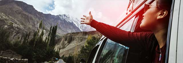 Junge Frau streckt sehnsuchtsvoll Richtung Berge die Hände aus dem Autofenster