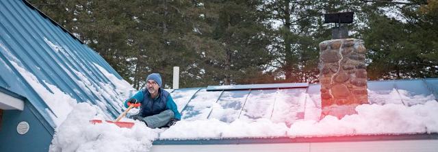 Mann schippt Schnee vom Dach