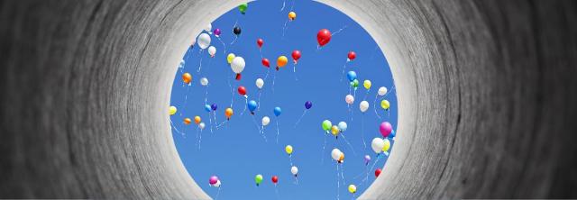 Am Ende eines Tunnels fliegen bunte Luftballons in den blauen Himmel