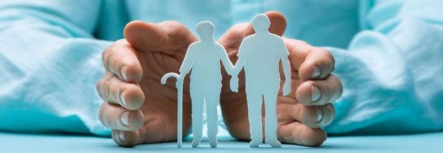 Seniorenpaar als Ausschneidefiguren wird von zwei Händen geschützt