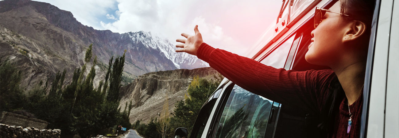 Junge Frau streckt sehnsuchtsvoll Richtung Berge die Hände aus dem Autofenster