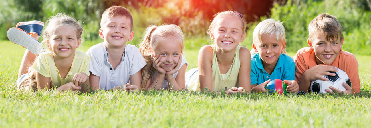 Sechs Kinder mit Fußball liegen auf einer Sommerwiese