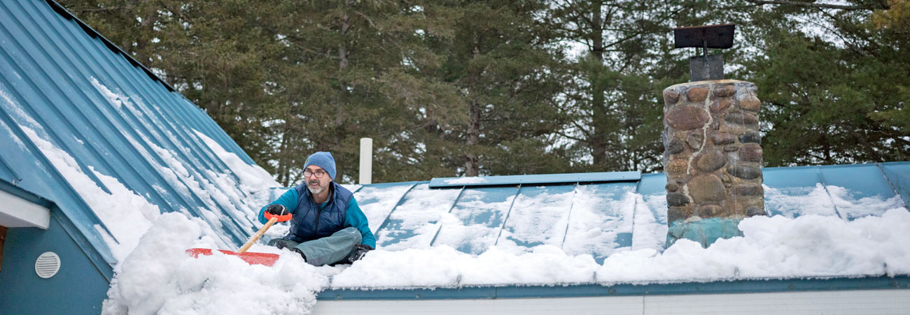 Mann schaufelt Schnee vom Hausdach