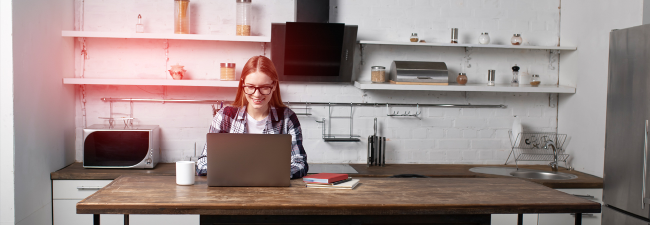 Junge Frau arbeitet am Kuechentisch am Laptop