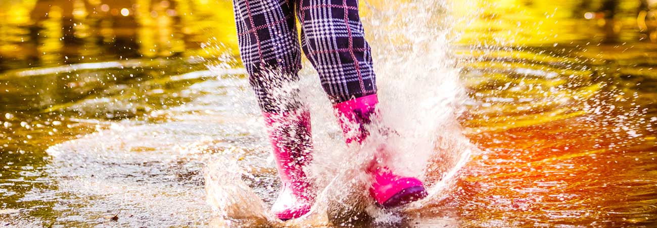 Kind läuft in Gummistiefeln durch Regenpfütze