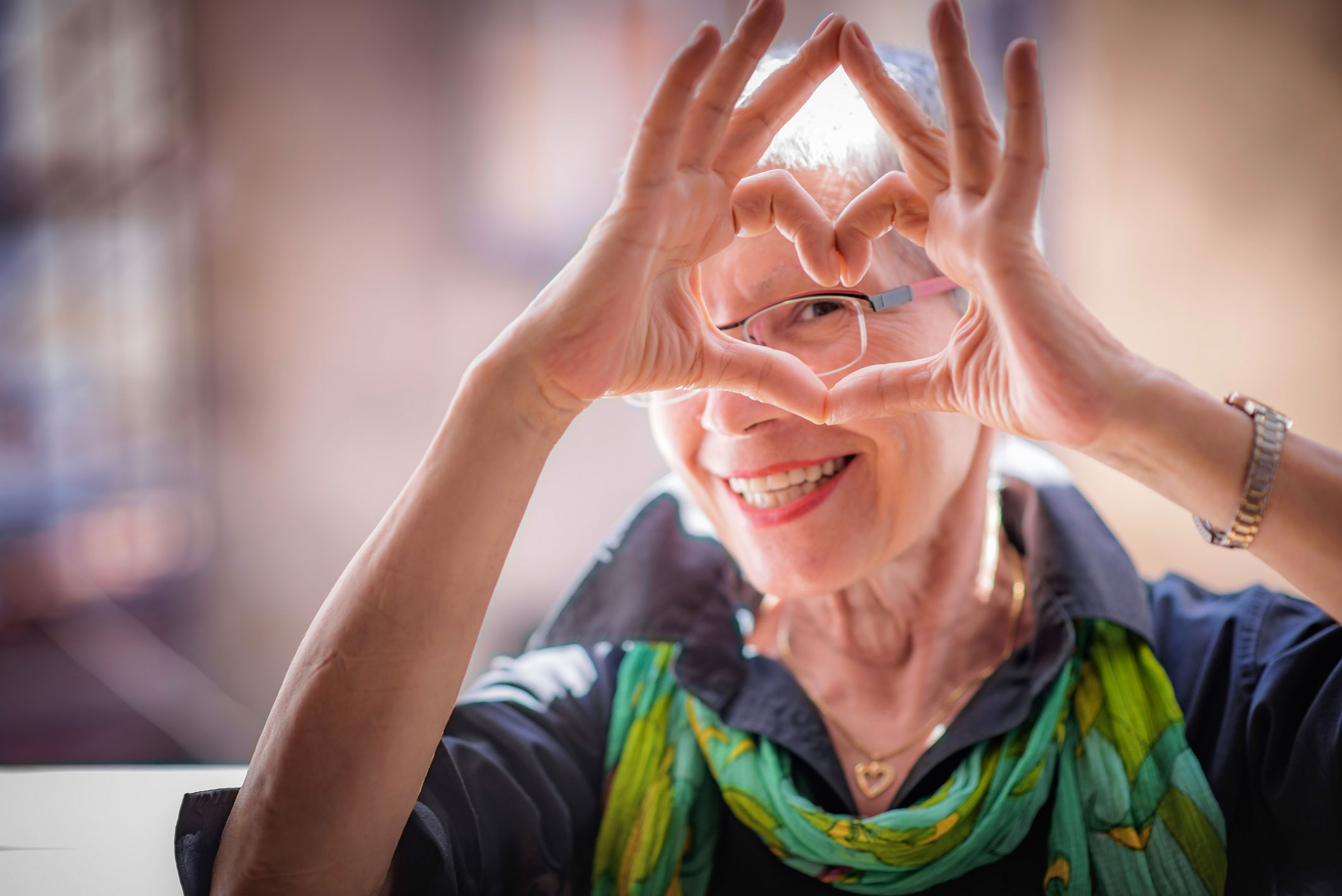 Ältere Frau Frau lächelt in die Kamera und formt ihre Hände zu einem Herz