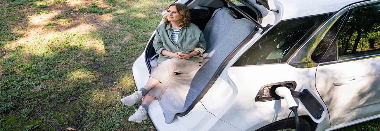  Frau sitzt im Kofferraum eines E-Auto, das lädt