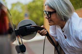 Seniorin bereitet E-Auto zum Laden vor