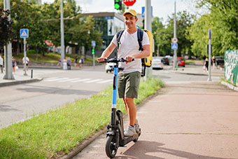 Mann fährt bei Tageslicht in einer Stadt mit einem E-Scooter auf einem Weg entlang