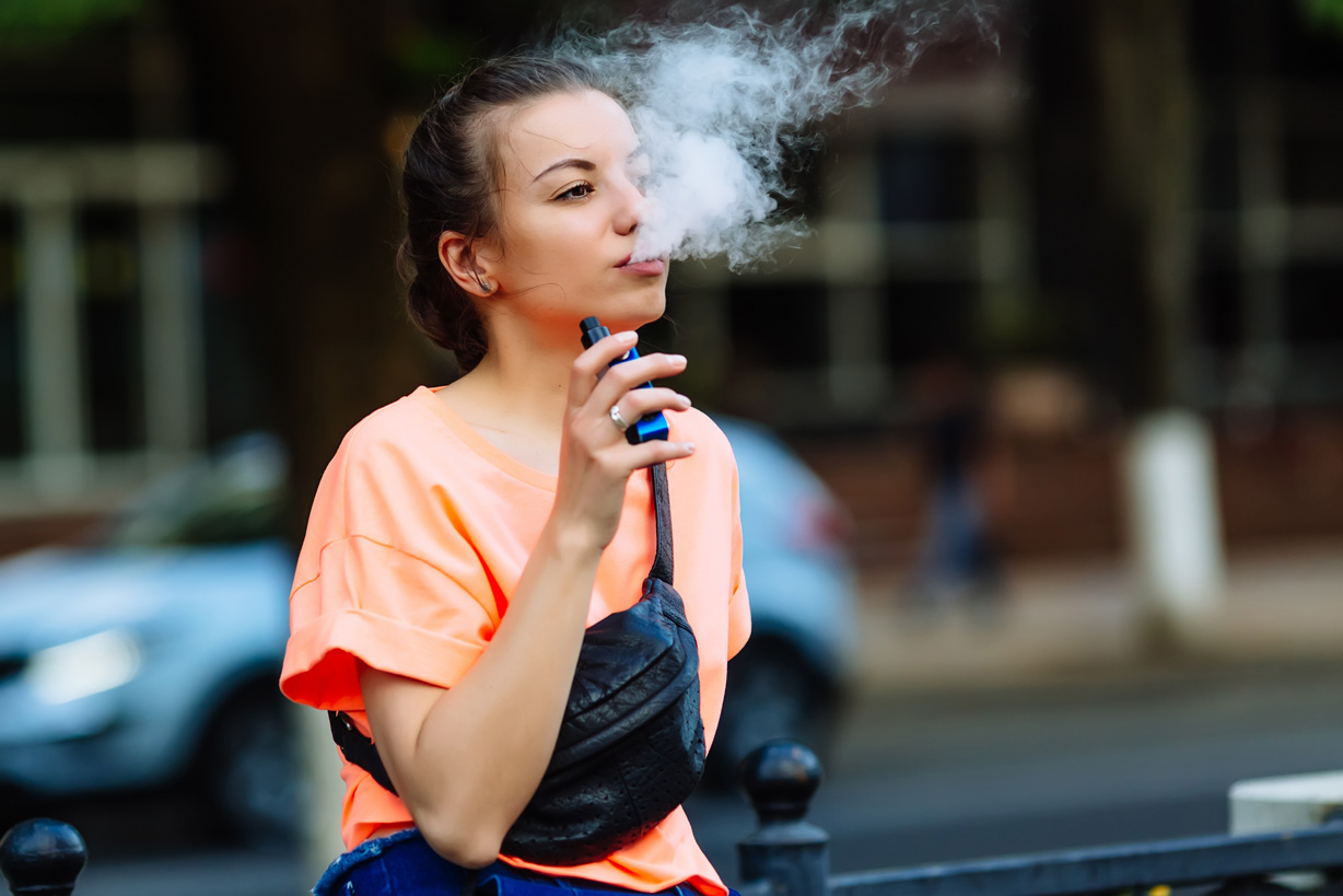 Junge Frau dampft eine Einweg-E-Zigarette