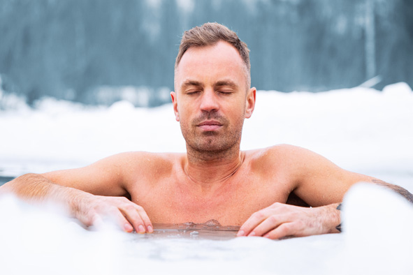 Mann entspannt beim Eisbaden in winterlicher Landschaft, Kopf und Oberkörper im kalten Wasser