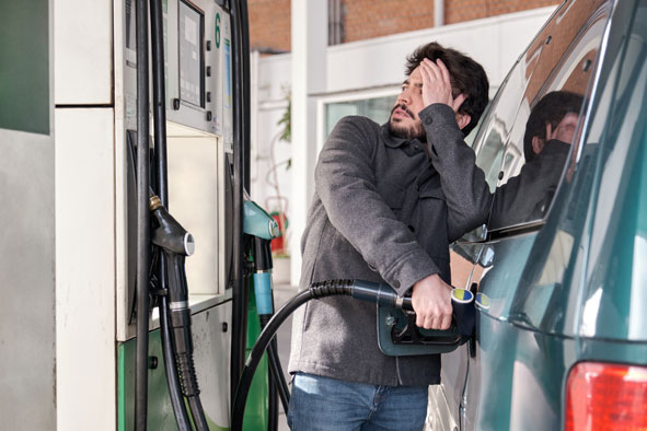 Mann betankt Auto, schaut sorgenvoll zur Zapfsäule