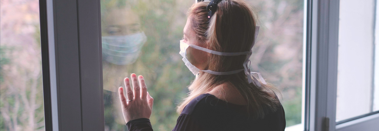 Junge Frau mit Maske am Fenster