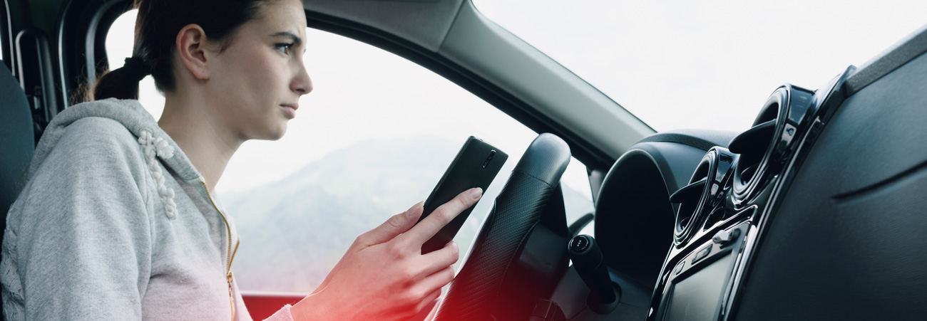 Junge Frau am Steuer eines Autos hält Smartphone in der Hand.
