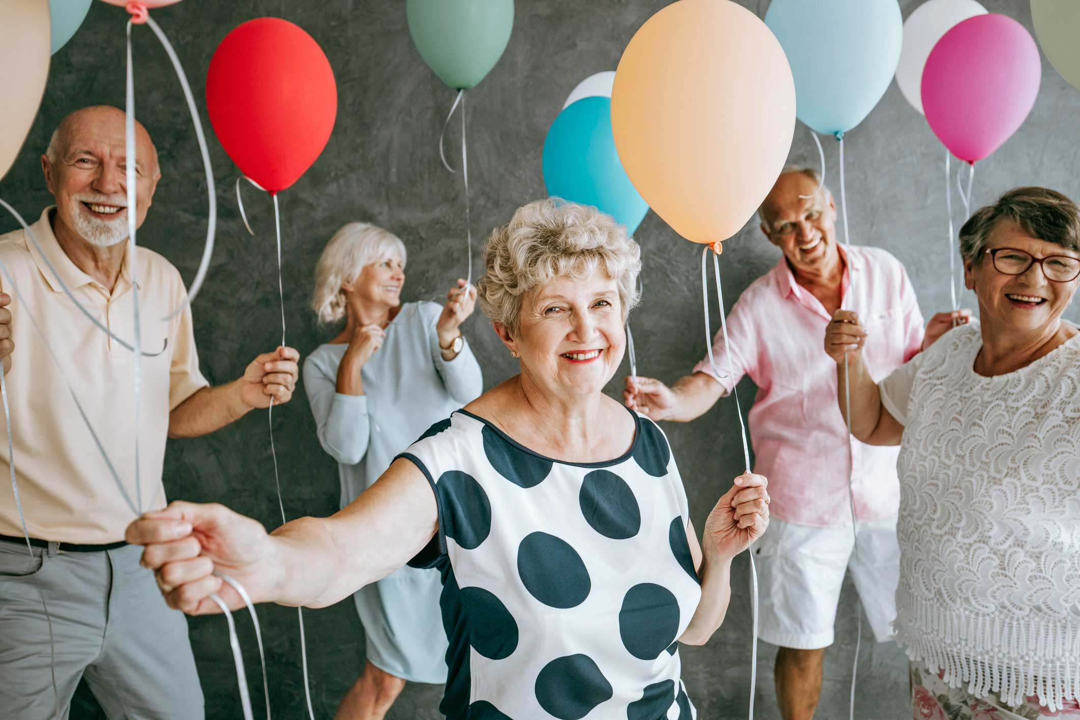 ältere Menschen halten lächelnd Luftballons
