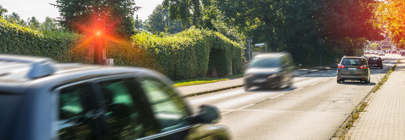 Fahrendes Auto wird von einer Radarkontrolle geblitzt, die rot aufleuchtet.