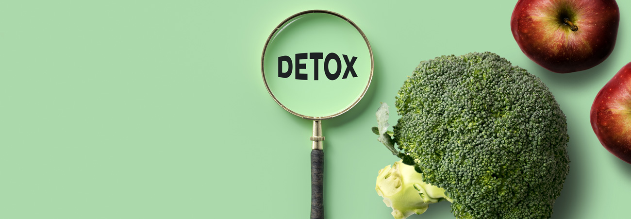 arrangement aus brokkoli, aepfeln und einer lupe üeber dem wort detox