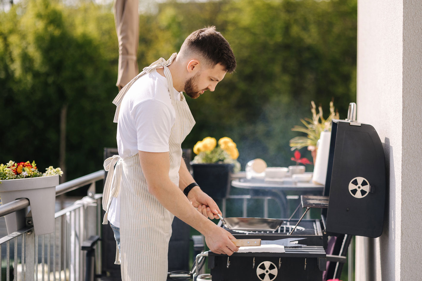 Mann steht auf Balkon an einem Gasgrill mit Deckel
