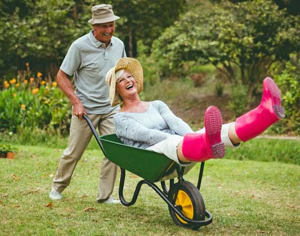 Mann fährt Frau in der Schubkarre durch den Garten