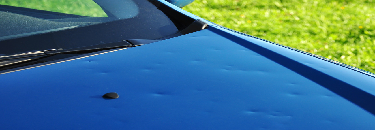 hagelschaden-eingedellte Motorhaube eines blauen Autos 