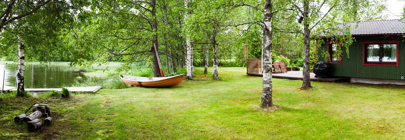 Ein grünes Holzferienhaus steht romantisch am See.