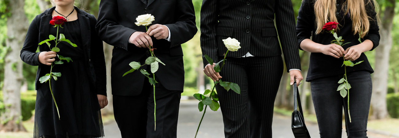 Trauernde Hinterbliebene mit Rosen in der Hand.