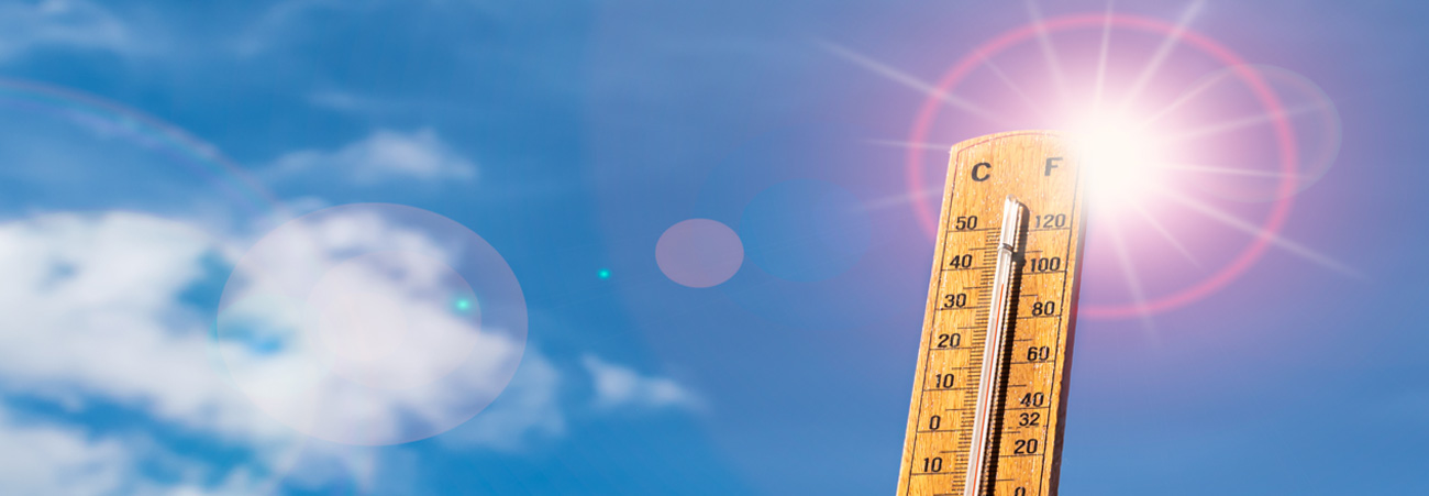 Thermometer vor blauem Sommerhimmel mit glühender Sonne.