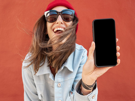 Hippe junge Frau mit Sonnenbrille zeigt ihr Smartphone