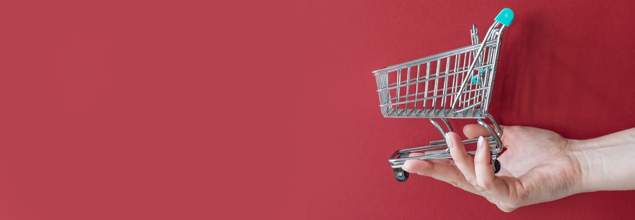 Eine Hand hält einen leeren Einkaufswagen vor rotem Hintergrund.