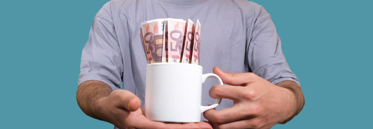 Mann hält Tasse in den Händen, in der viele 50-Euro-Scheine stecken.