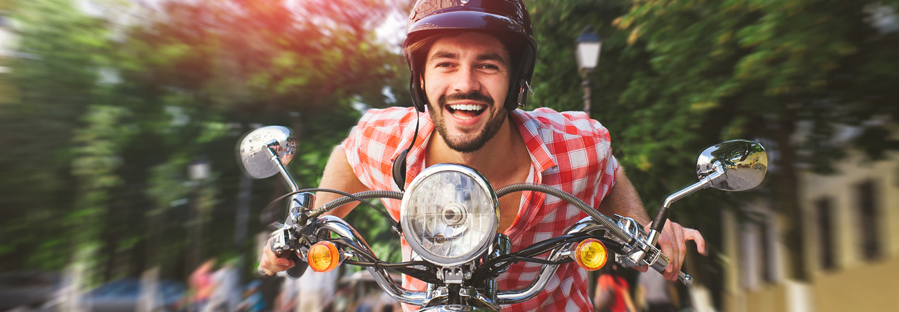 Lachender, junger Mann fährt auf einem Moped.