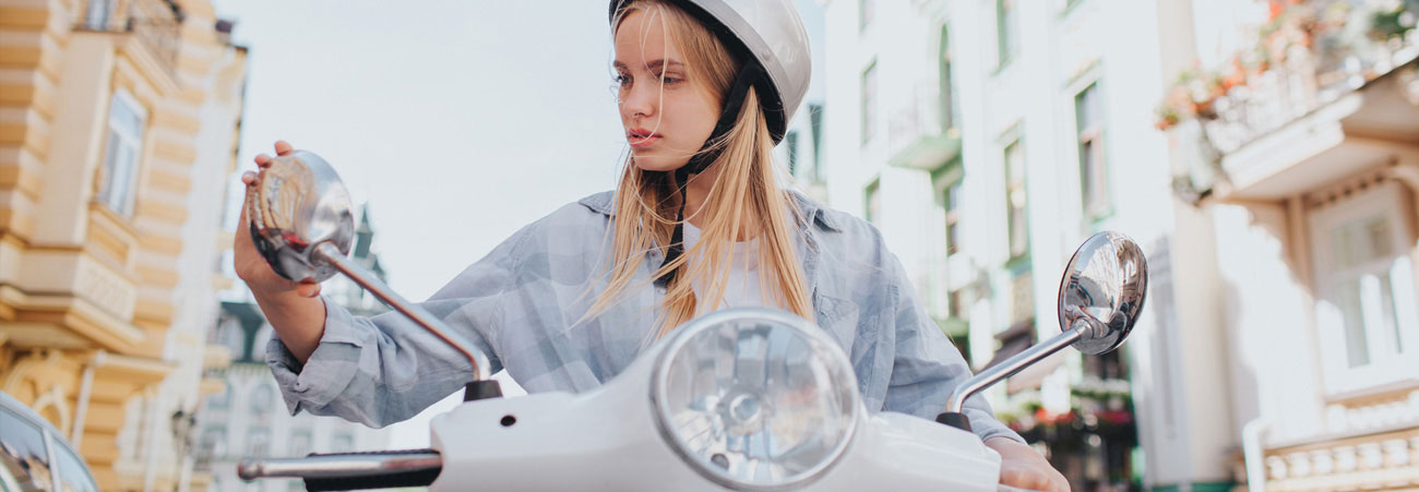 Junges, blondes Mädchen sitzt auf einem Motorroller.